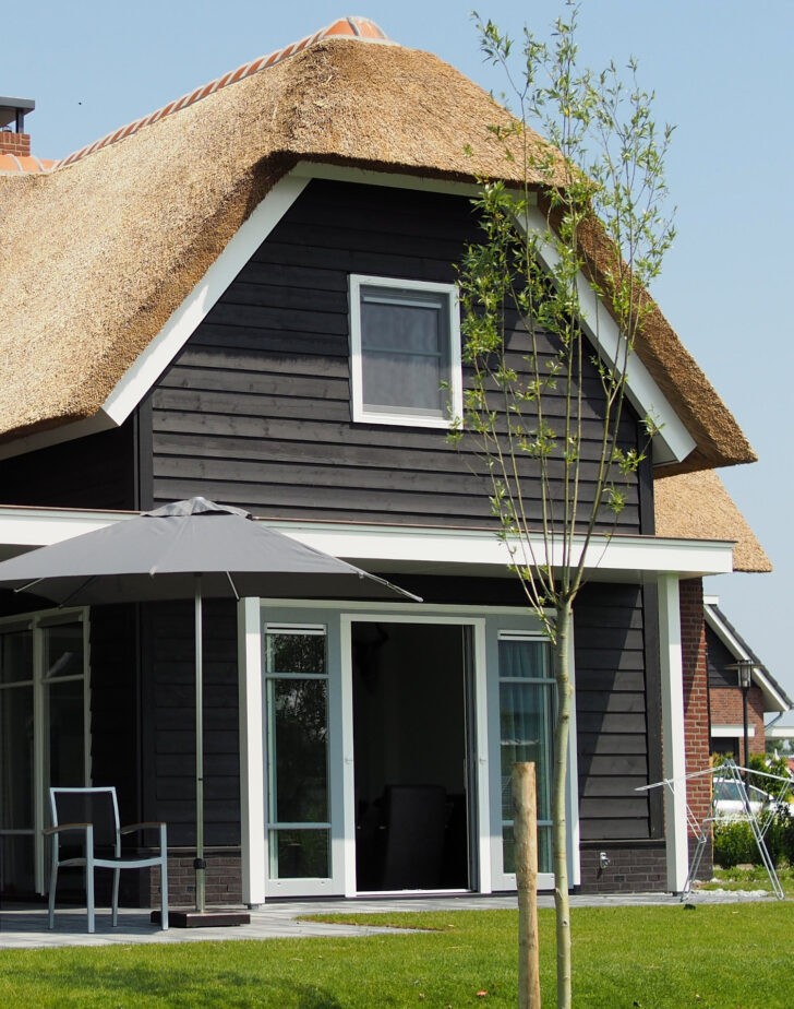 Casa de madera con techo de paja y paredes negras o grises oscuro