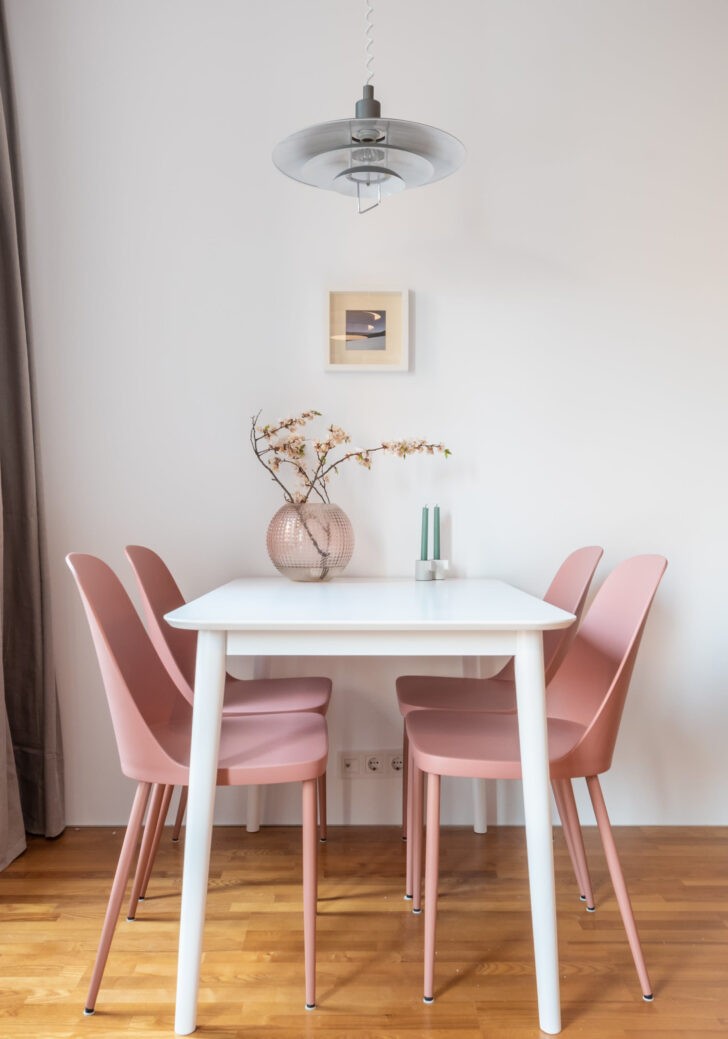 Sillas rosadas y mesa de comedor sencilla, junto a la pared blanca en la decoración del monoambiente 