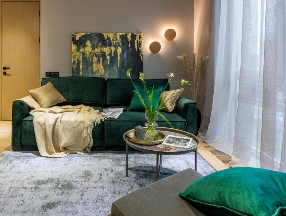 Salón de color gris con sillón verde oscuro y cojines verde esmeralda