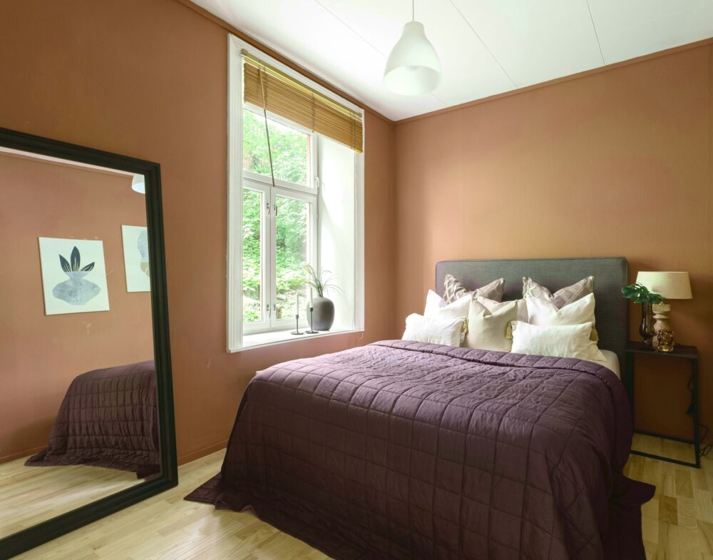 Dormitorio pequeño pintado de color terracota y cama oscura