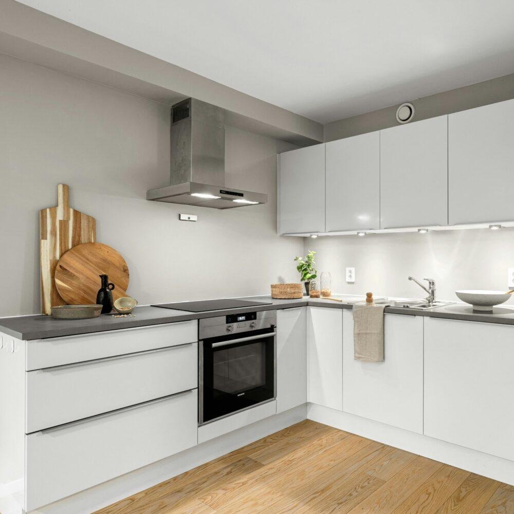 Cocina en L con paredes en gris claro y muebles lacados en blanco