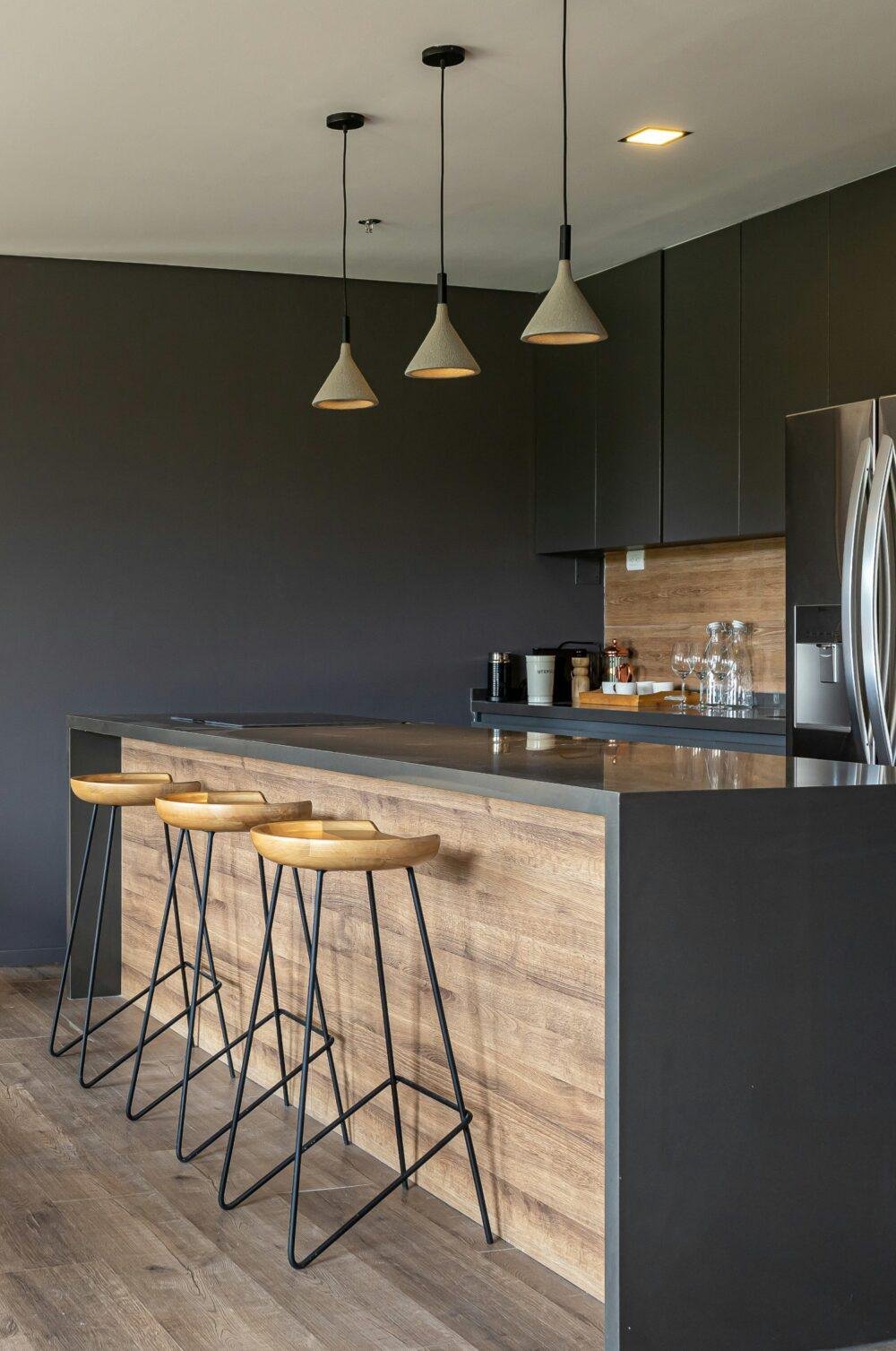Una cocina con muebles y paredes en gris oscuro grafito y madera con una gran isla central